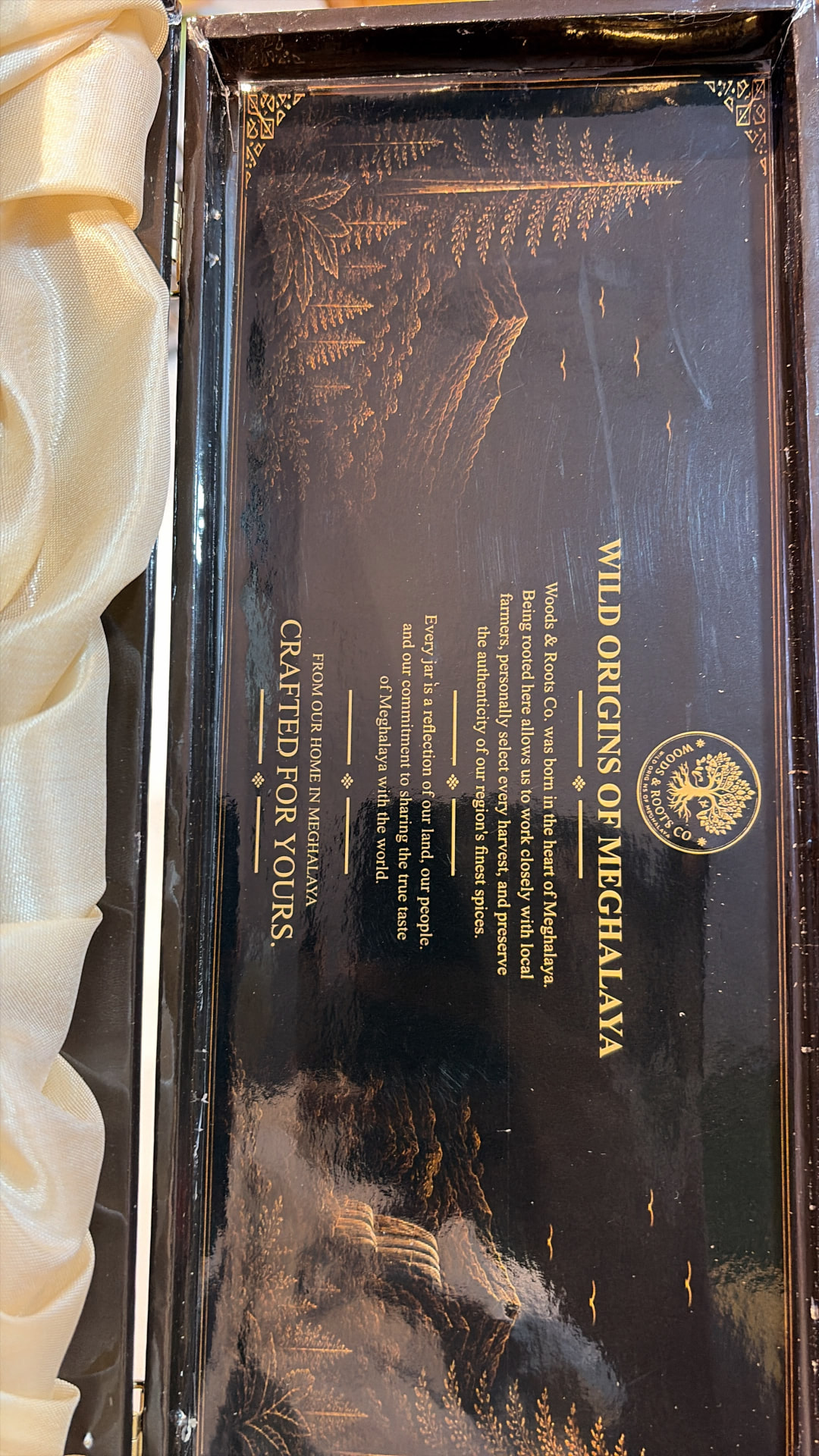 Inside lid of the Woods & Roots gift box with gold tree logo and Wild Origins of Meghalaya story